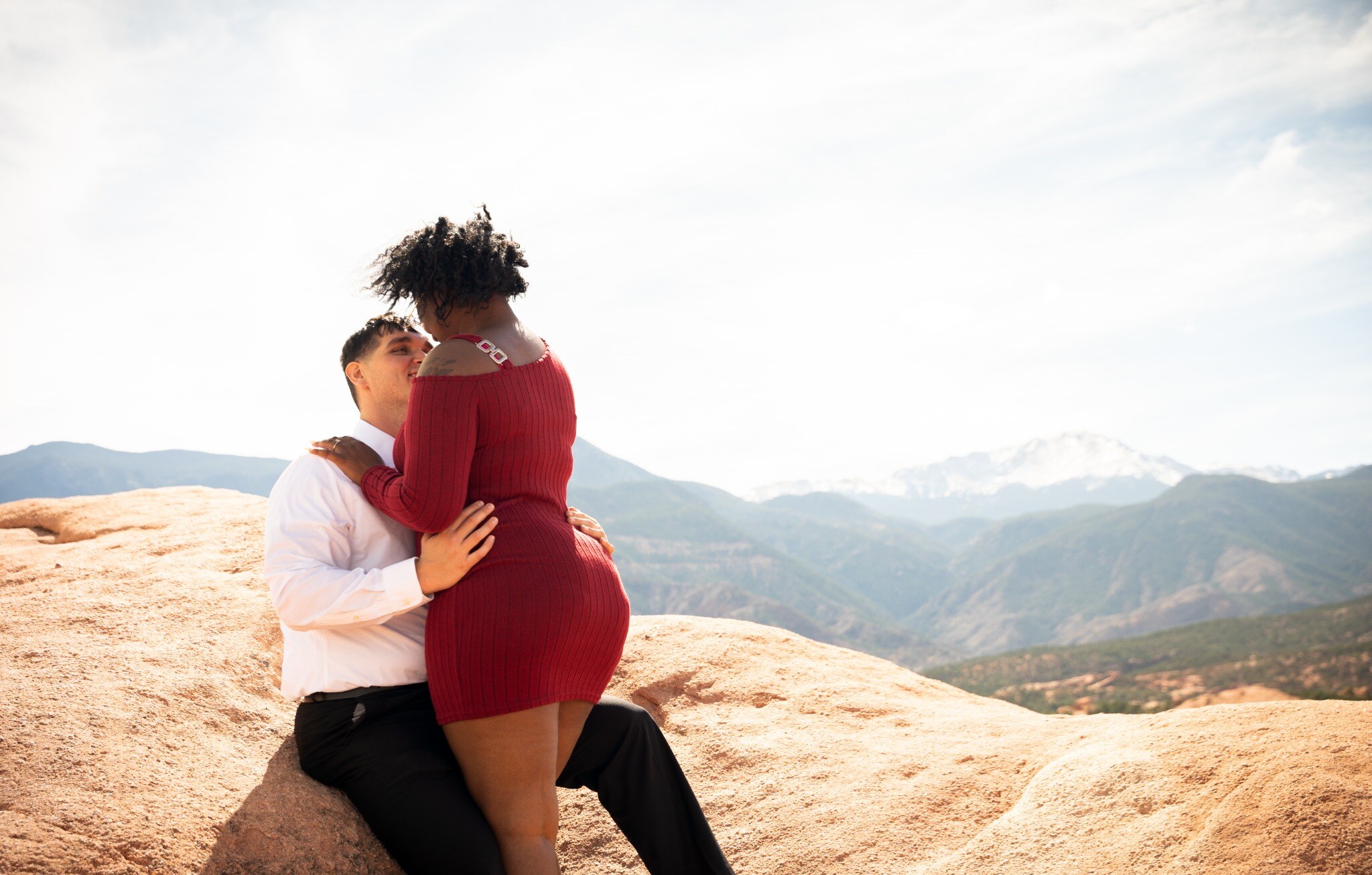 Engaged couple embracing on red rocks with Colorado mountain views