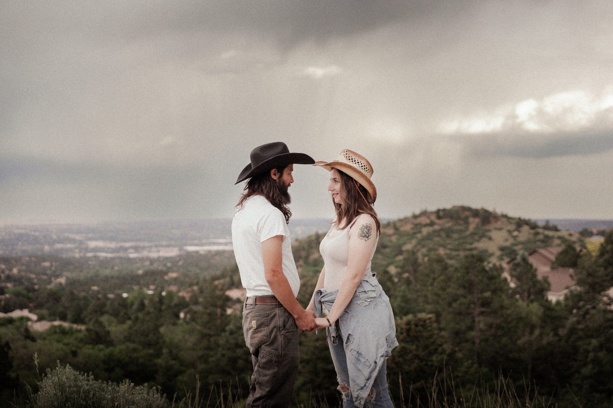 Western couple holding hands beneath a dramatic Colorado sky