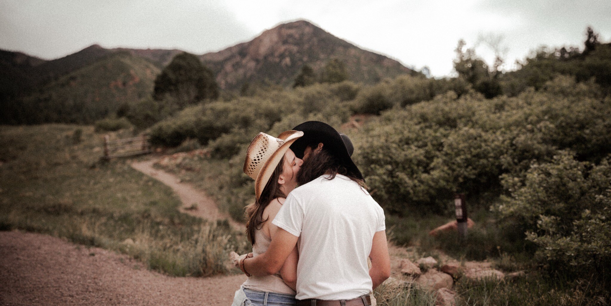 Cowboy-hat couple kissing on a mountain trail